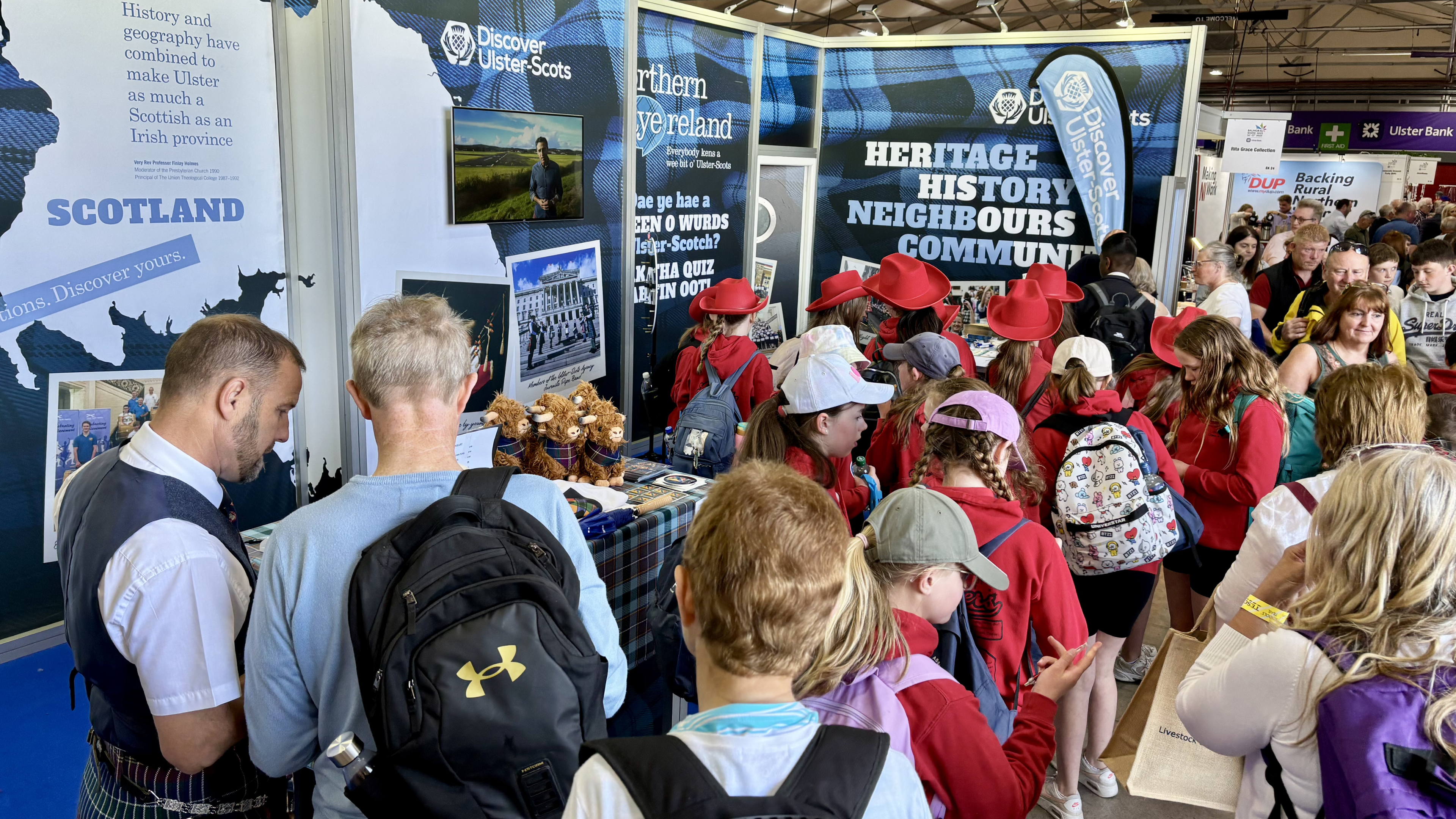 Crowd of people exploring Ulster-Scots heritage and history exhibition booth with informational displays and souvenirs.