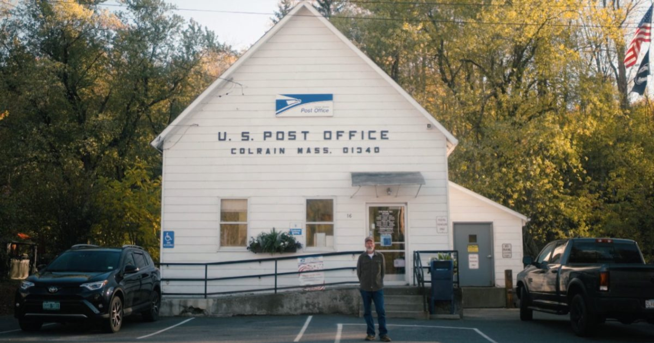 Small white U.S. Post Office building in Colrain, Massachusetts, surrounded by autumn trees and parked cars.
