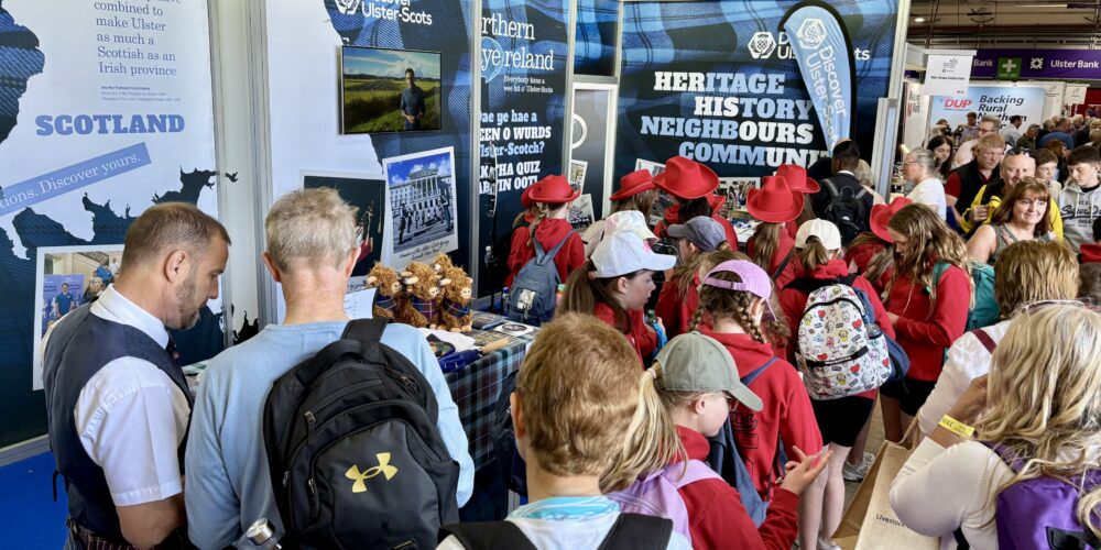 Crowd of people exploring Ulster-Scots heritage and history exhibition booth with informational displays and souvenirs.