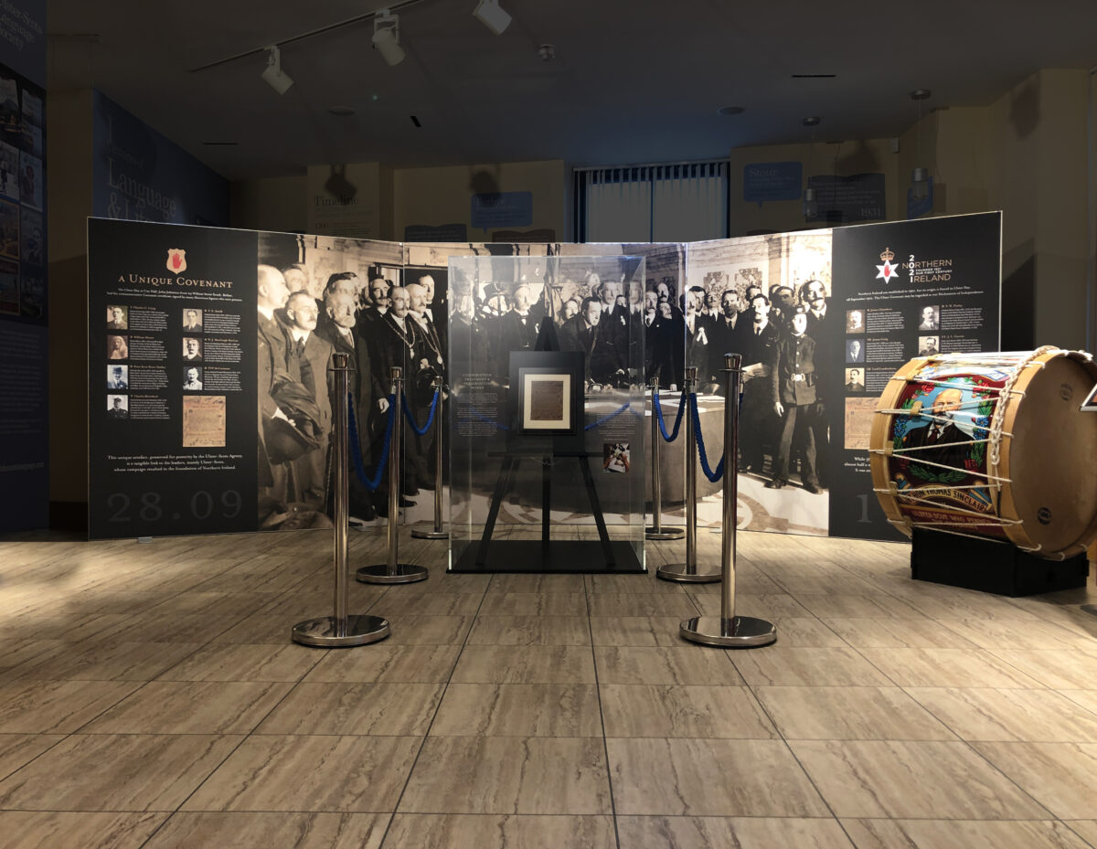 Museum exhibit featuring a historical black-and-white photo of a group of men, with informational panels in the background and a Lambeg drum on the right.