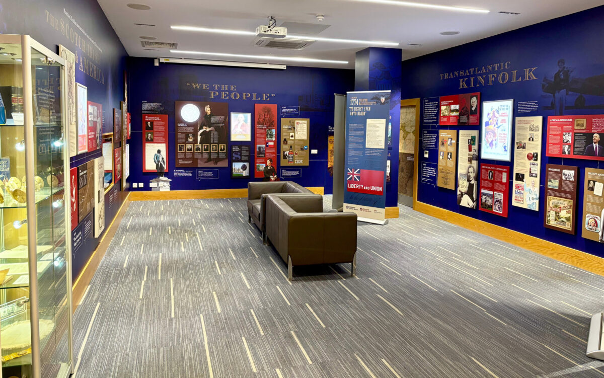 Interior view of a museum gallery with blue walls featuring historical exhibits and informational panels about 'Scotch-Irish in America' and 'Transatlantic Kinfolk'.