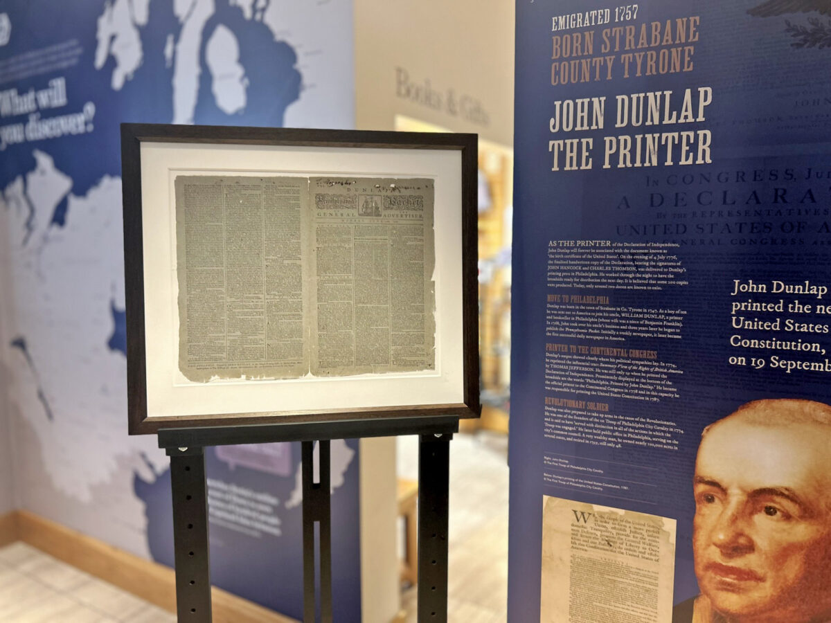 Framed historical newspaper, The Pennsylvania Packet, displayed on a stand in a museum exhibit about John Dunlap, the printer of the U.S. Constitution.