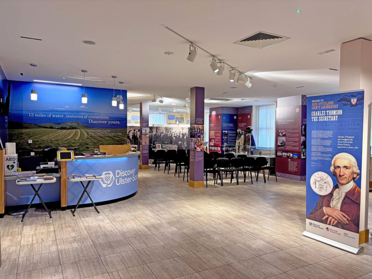 Interior of the Discover Ulster-Scots Centre, a modern visitor centre with a blue reception desk, grey floor, and informational displays about local heritage.
