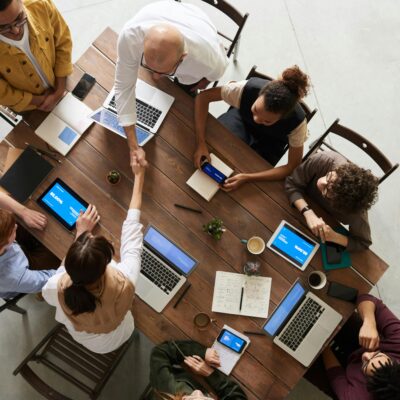Several people working on computers at a table, two of which are shaking hands