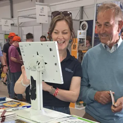 A man and a woman interact with a touchscreen display at a busy indoor exhibition booth.