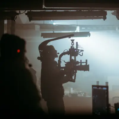 Silhouetted camera operator filming with a stabiliser rig in a dimly lit, foggy indoor set.