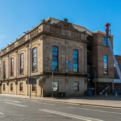 Historic stone building, The Corn Exchange in Belfast, with large windows under a clear blue sky on a quiet street.