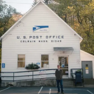 Small white U.S. Post Office building in Colrain, Massachusetts, surrounded by autumn trees and parked cars.