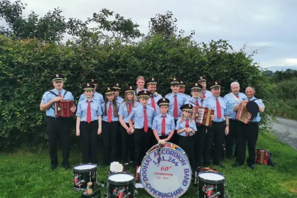 A group of musicians in uniform standing outdoors with various instruments including accordions and drums.