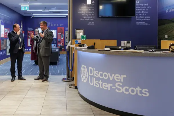 Reception area of Discover Ulster-Scots Centre in Belfast with two men conversing near the entrance and informational displays on the walls.