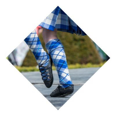 Close-up of a highland dancer's legs wearing blue and white argyle knee-high socks and traditional black ghillie shoes on a wooden stage.