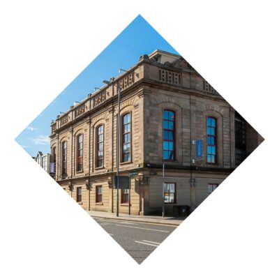 Historic stone building, The Corn Exchange in Belfast, with large windows under a clear blue sky on a quiet street.